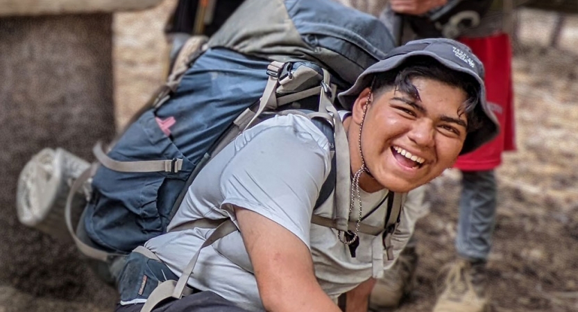 a student wearing a backpack laughs on a outward bound backpacking trip